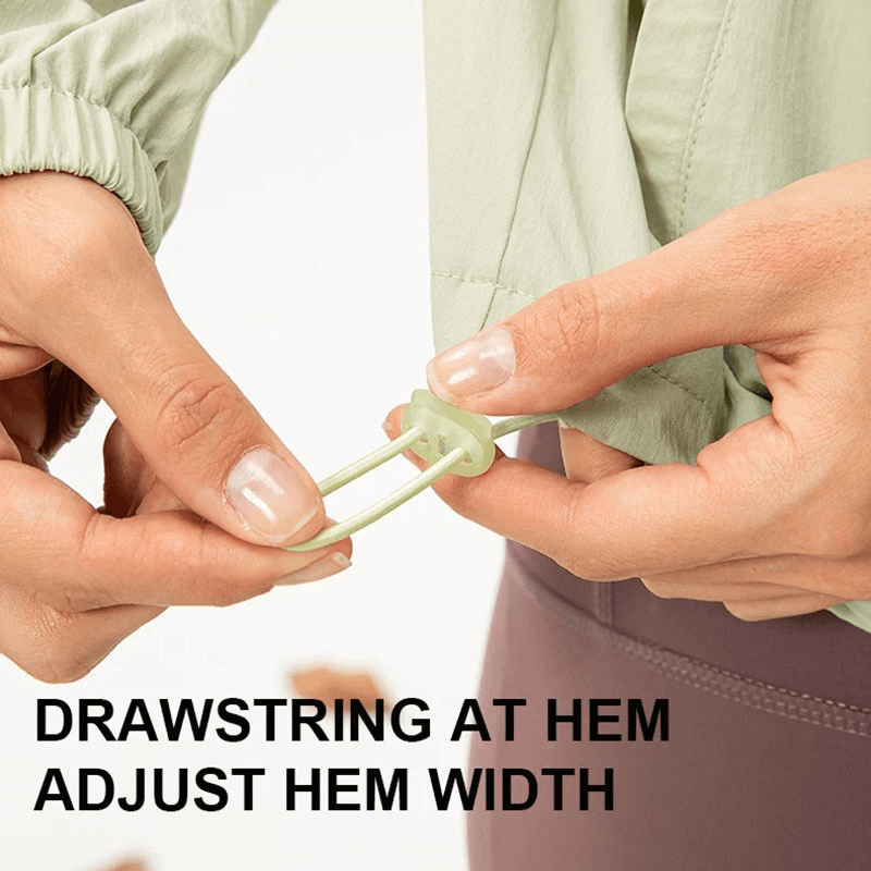 Close-up of hands adjusting drawstring at the hem of a women's running windbreaker for customizable fit.